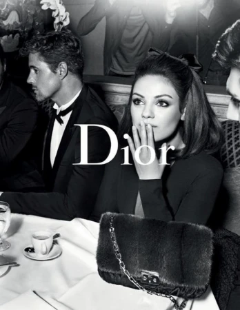 Black and white fashion shot of woman in black dress with fur purse, and man in tuxedo at table with drinks for a Dior ad.