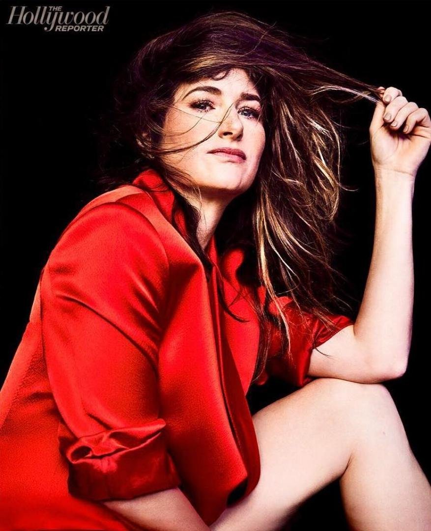 Kathryn Hahn wearing a red silk shirt in a close portrait with tousled hair against a black background