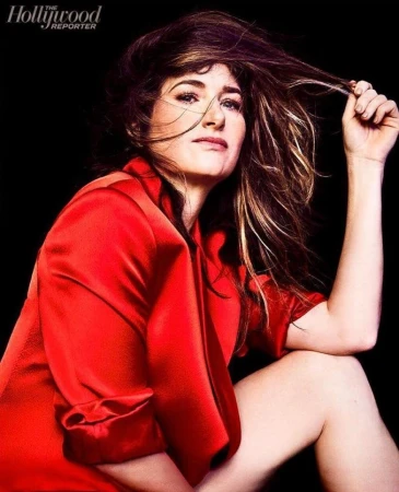Kathryn Hahn wearing a red silk shirt in a close portrait with tousled hair against a black background