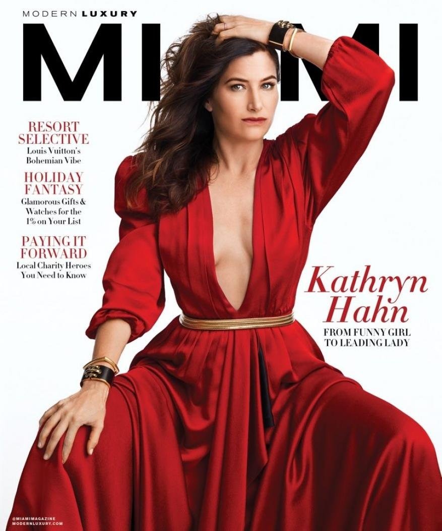 Kathryn Hahn magazine cover portrait. Adult woman in a red dress poses with bracelets in an indoor studio environment on a white background.