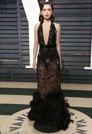 Woman in elegant black gown with a plunging neckline, posing on a circular patterned carpet against a paneled wall backdrop.