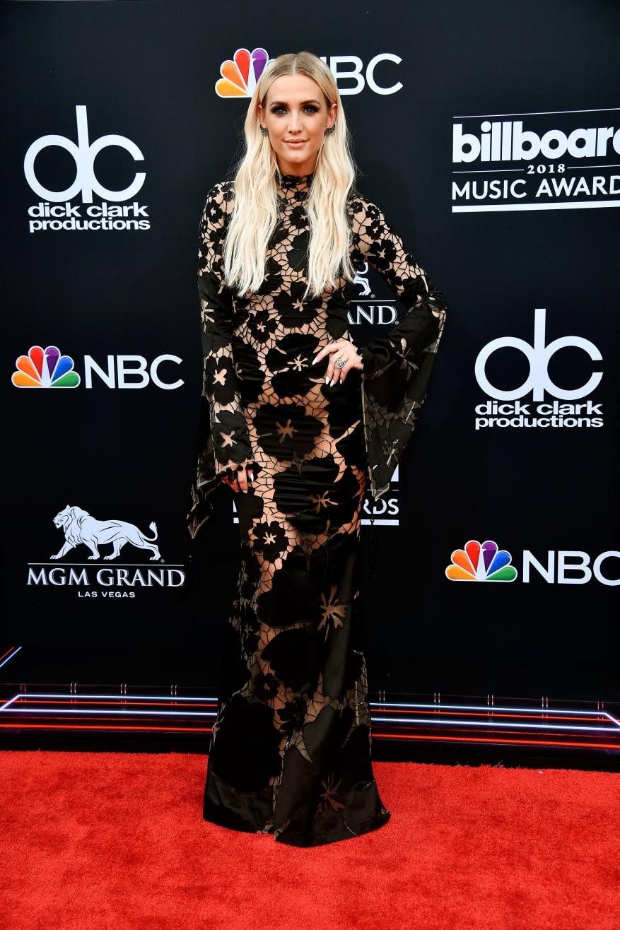 Ashlee Simpson Ross poses in a black floral lace gown on a red carpet at the 2018 Billboard Music Awards, wearing a floor-length gown.