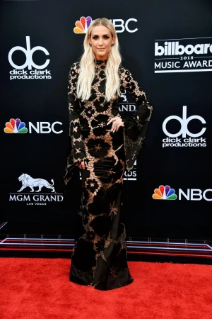 Ashlee Simpson Ross poses in a black floral lace gown on a red carpet at the 2018 Billboard Music Awards, wearing a floor-length gown.