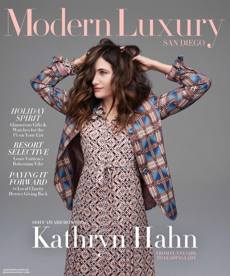 Kathryn Hahn on the cover of Modern Luxury San Diego magazine, wearing a patterned dress and jacket, with her hands in her hair.