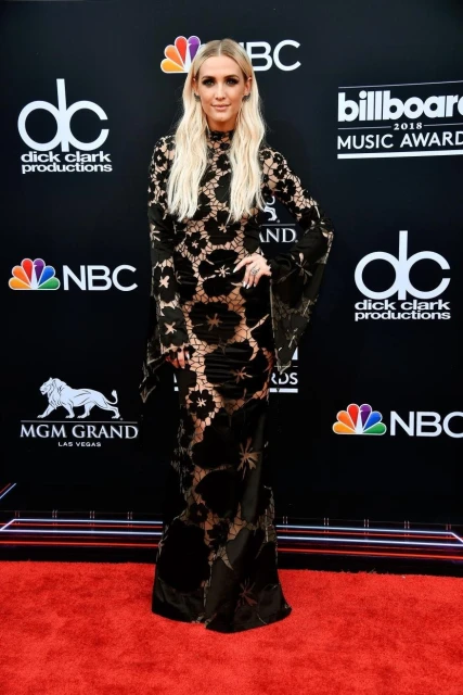 Ashlee Simpson poses in a long black lace gown on the red carpet at the Billboard Music Awards. She has long blonde hair.