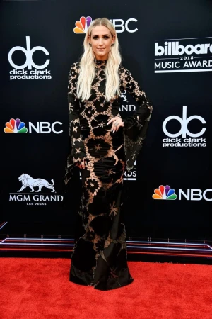 Ashlee Simpson poses in a long black lace gown on the red carpet at the Billboard Music Awards. She has long blonde hair.