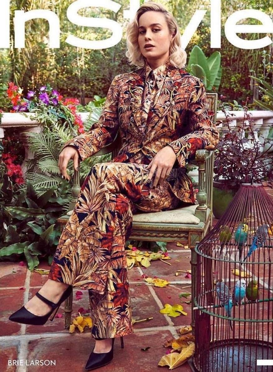 Brie Larson on the cover of InStyle magazine, sitting in a chair wearing a leaf-patterned suit, with a birdcage nearby.
