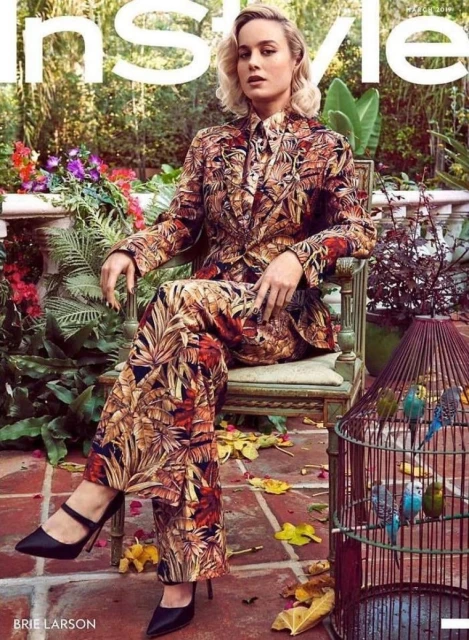 Brie Larson on the cover of InStyle magazine, sitting in a chair wearing a leaf-patterned suit, with a birdcage nearby.