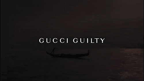 Dark, moody shot of a gondola silhouetted on calm water with the words 'GUCCI GUILTY' in white text at the center of the frame.