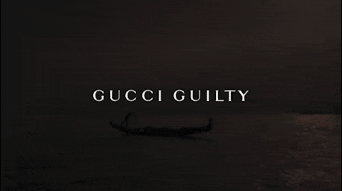 Dark, moody shot of a gondola silhouetted on calm water with the words 'GUCCI GUILTY' in white text at the center of the frame.