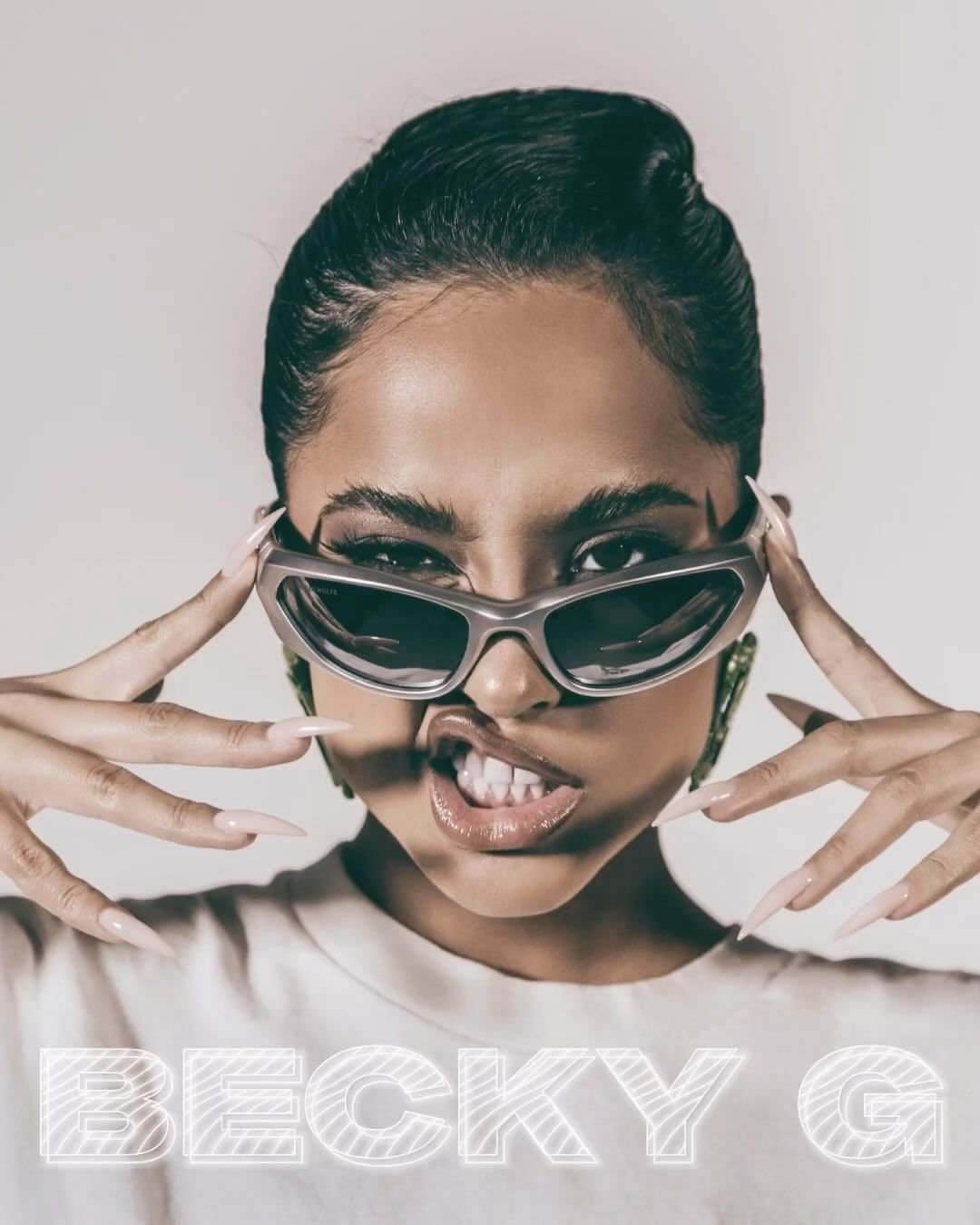 Close-up portrait of Becky G wearing sunglasses and a white t-shirt against a light background with text overlay.