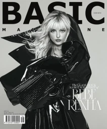 Bebe Rexha wearing a shiny black vinyl coat with dramatic lapels against a plain grey backdrop for a magazine cover