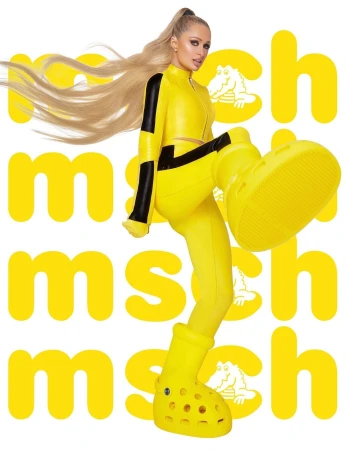 Paris Hilton poses in bright yellow outfit and oversized Crocs, a fashion-forward and playful image against a logo background.