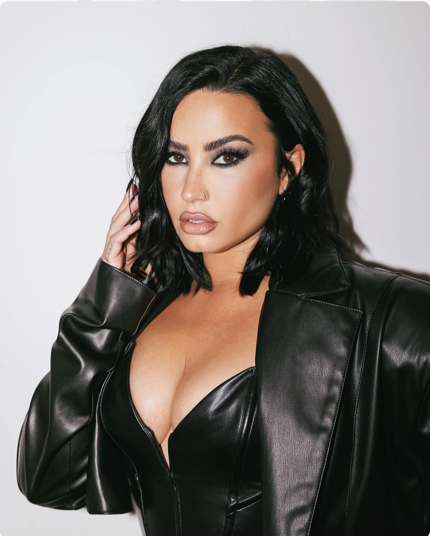 Portrait of an adult female with dark hair, wearing a black leather jacket and eye makeup, posing against a neutral background.