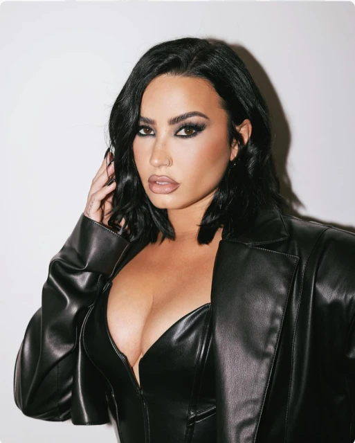 Portrait of an adult female with dark hair, wearing a black leather jacket and eye makeup, posing against a neutral background.