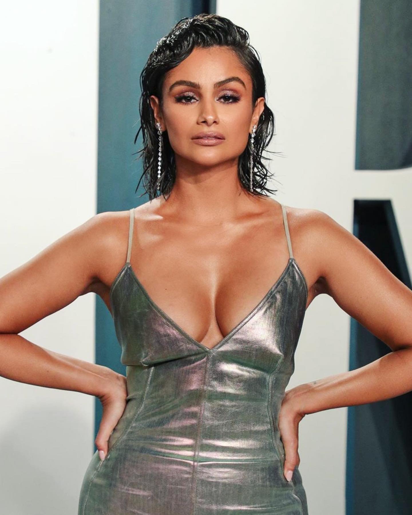 Portrait of a woman with wet-look dark hair wearing a metallic spaghetti-strap dress and drop earrings