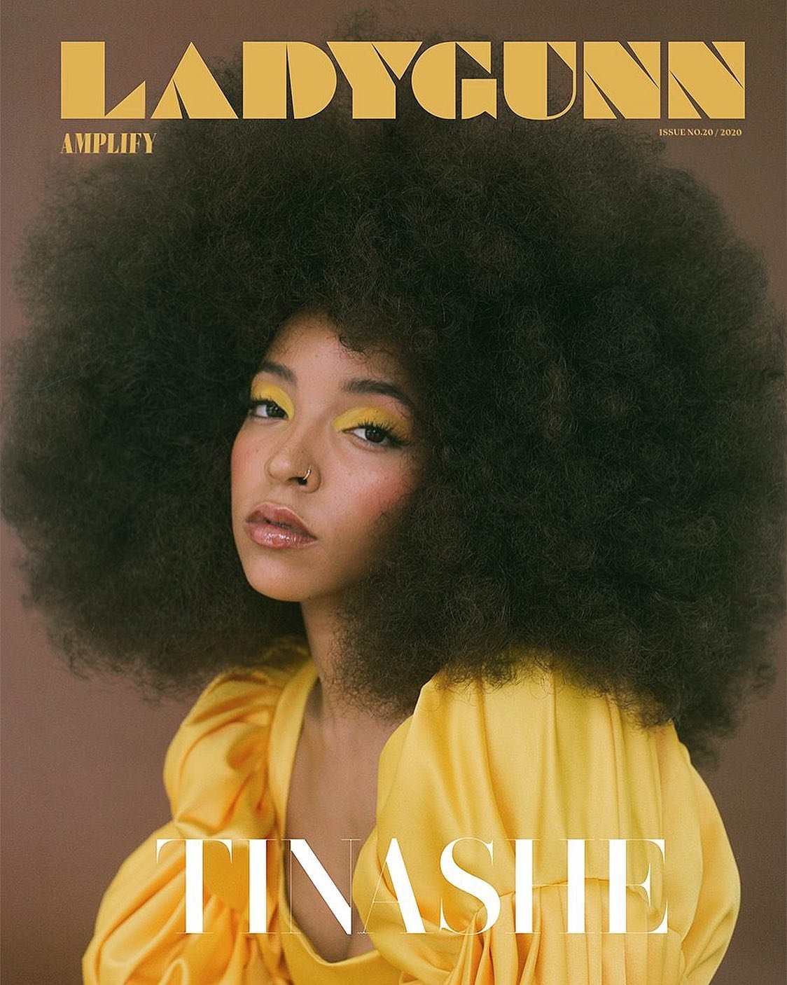 Magazine cover featuring a woman with a large afro hairstyle, yellow eyeshadow, and a yellow ruffled top against a neutral background.