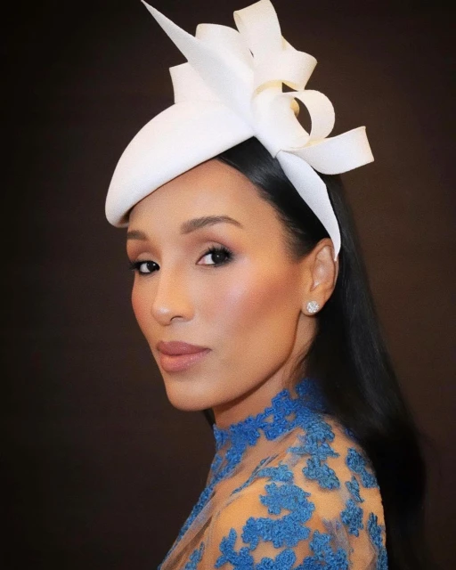 Elegant portrait of a woman with a white hat featuring ribbon detail and blue lace, set against a dark backdrop.