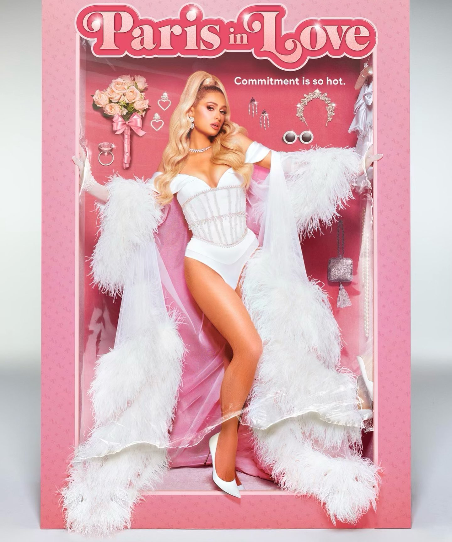 Paris Hilton appears as a doll in a pink toy box wearing a white outfit, a white robe with feathered trim, and matching heels.