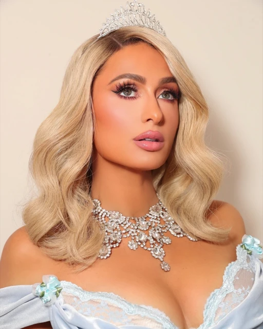 Close-up portrait of Paris Hilton in an off-the-shoulder dress, diamond tiara, and elaborate diamond necklace against a neutral backdrop.