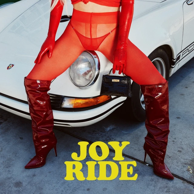 Woman in red latex gloves and boots poses on a white Porsche car with a small black purse, evoking a provocative and fashionable aesthetic.