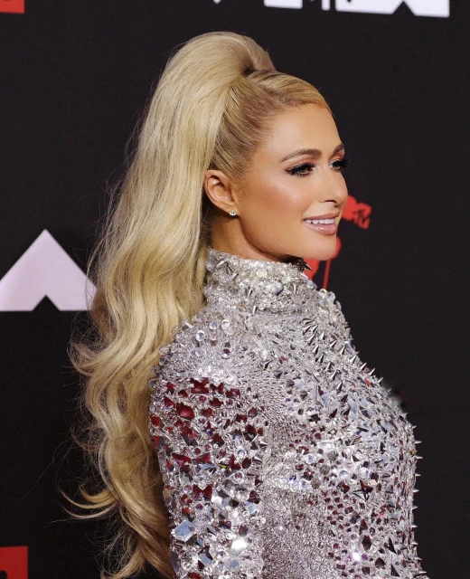 Profile portrait of Paris Hilton with a blonde ponytail and silver dress on a black background at the MTV Video Music Awards.