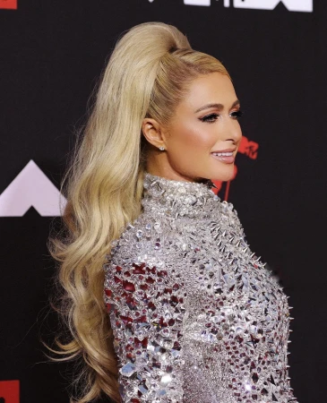 Profile portrait of Paris Hilton with a blonde ponytail and silver dress on a black background at the MTV Video Music Awards.
