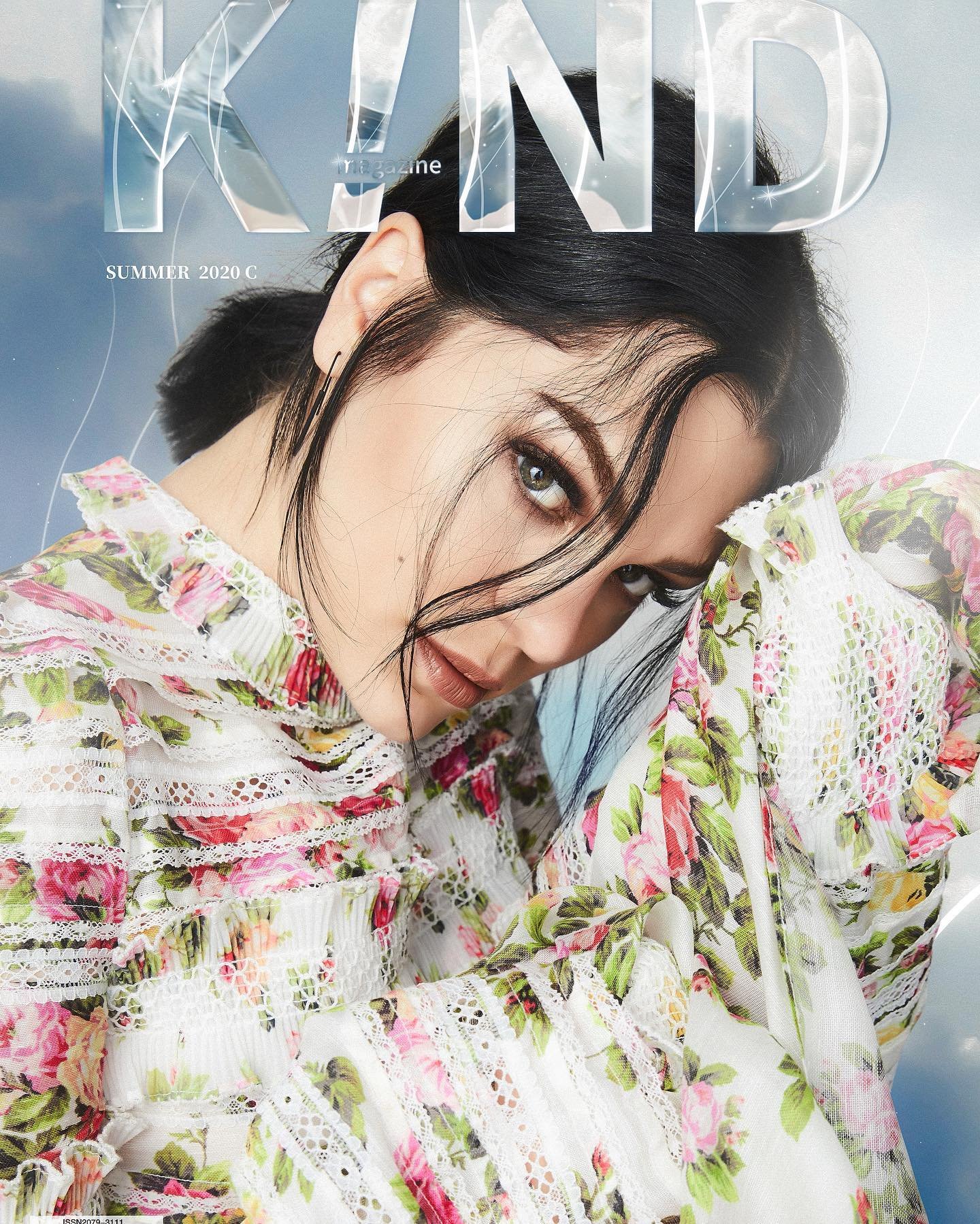 Magazine cover featuring a fair-skinned woman with dark hair in a floral blouse, posing against a blurred sky background with text overlay.