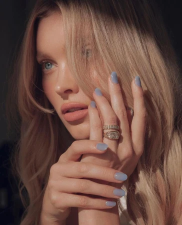 Close-up of a blonde woman with blue nail polish and jewelry; light skin, soft lighting, beauty shot with natural makeup.