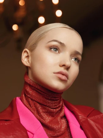 Close-up portrait of Dove Cameron with blonde hair wearing a sparkly red turtleneck and pink jacket by Elias Tahan.