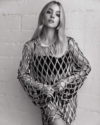 Portrait of a blonde woman wearing a shimmering netted top and rings against a painted brick wall, photographed by Elias Tahan.