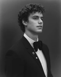 Portrait of a man with curly hair wearing a tuxedo and bow tie against a dark background, photographed by Elias Tahan.