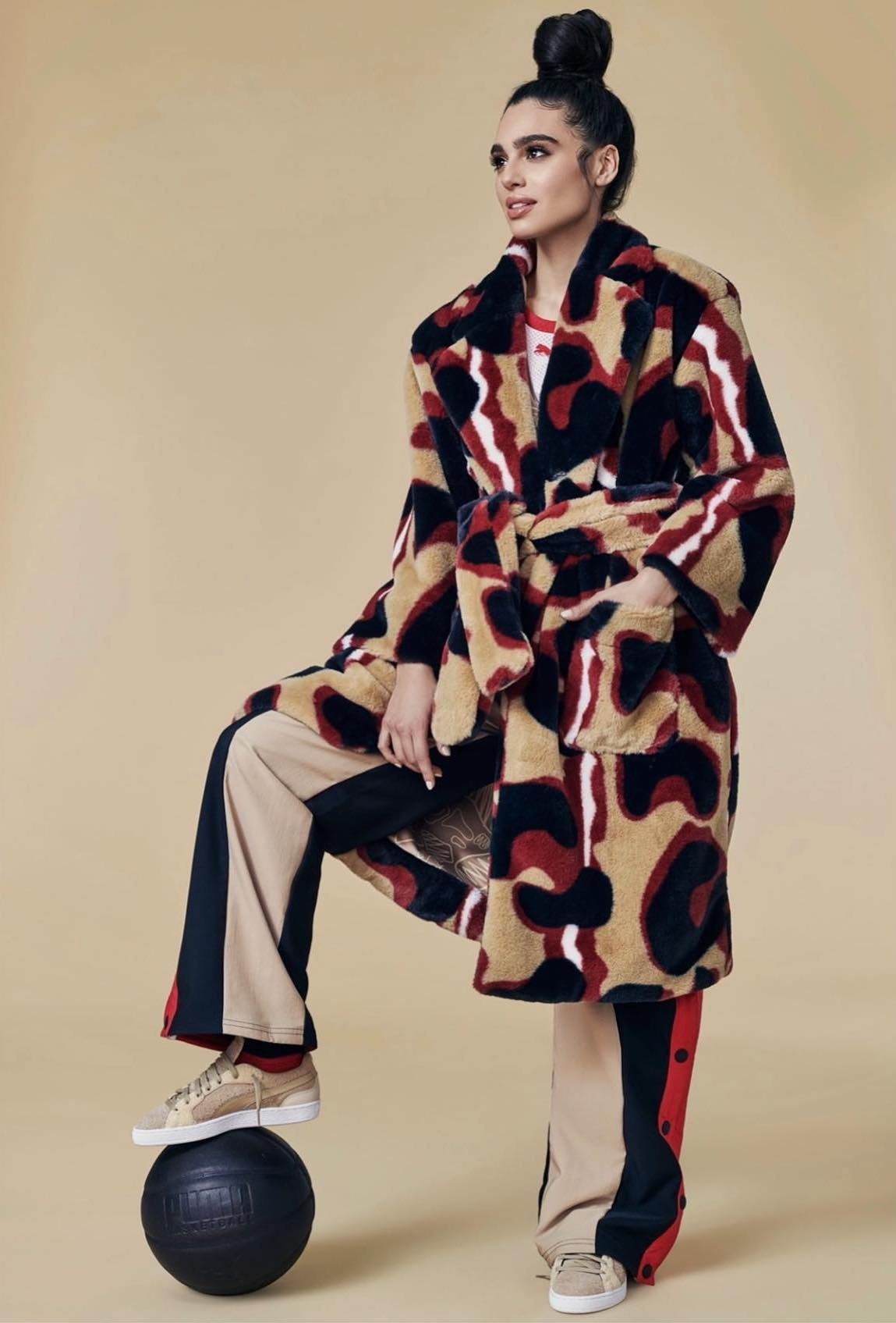 Fashionable woman in a patterned coat poses with a basketball in a studio, showcasing a blend of sporty and chic style.