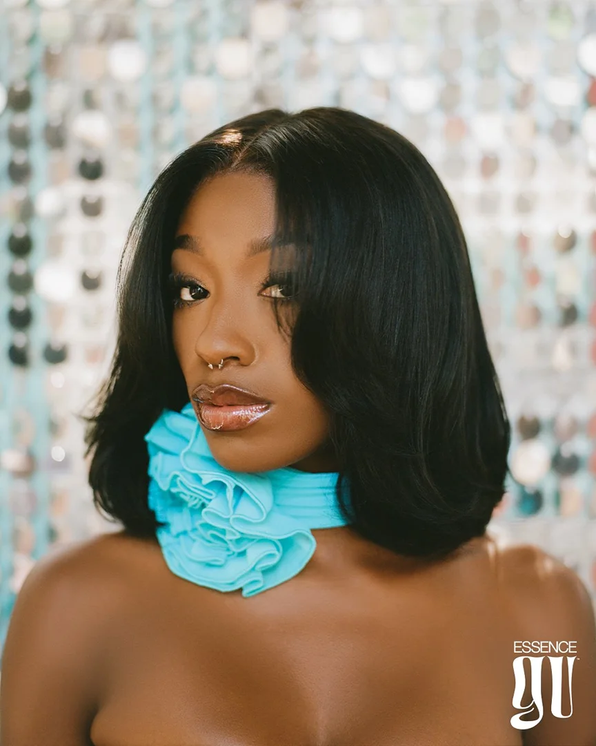 Close-up portrait of a woman with medium length black hair and a blue ruffled collar against a shimmering silver background.