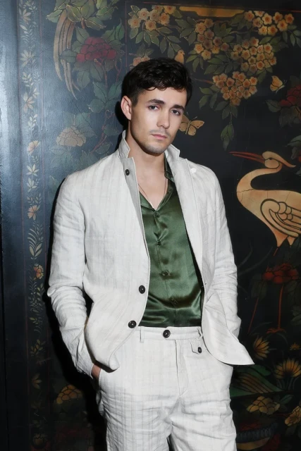 Man poses in an off-white suit against a dark floral backdrop, creating a fashionable and eye-catching portrait.