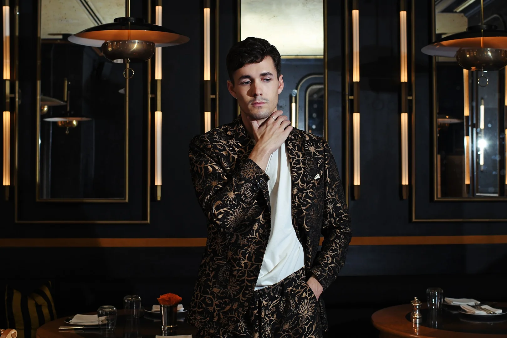 Portrait of a dark-haired adult male in patterned suit. He's posing in a restaurant setting with soft lighting and dark ambiance.
