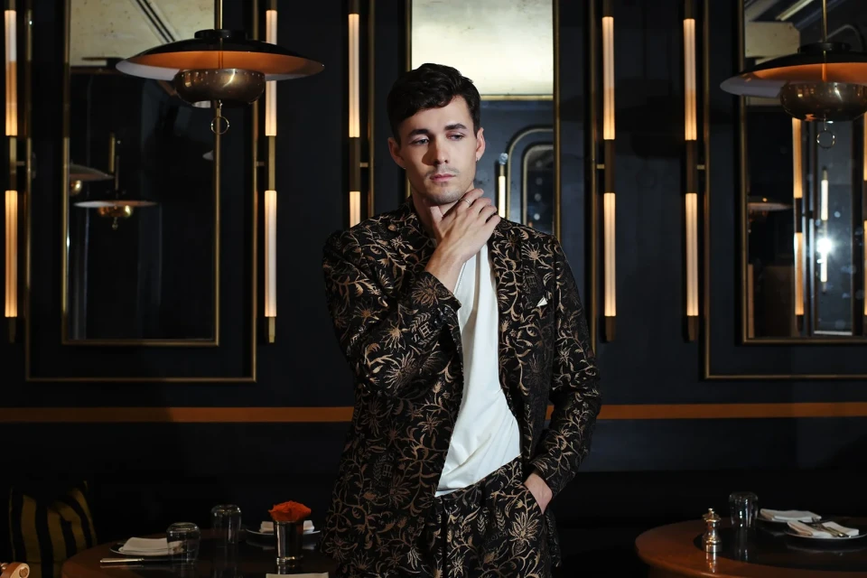 Portrait of a dark-haired adult male in patterned suit. He's posing in a restaurant setting with soft lighting and dark ambiance.