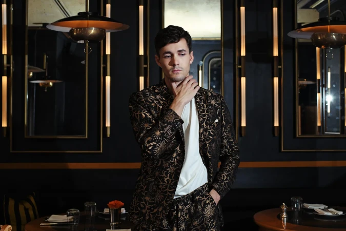 Portrait of a dark-haired adult male in patterned suit. He's posing in a restaurant setting with soft lighting and dark ambiance.