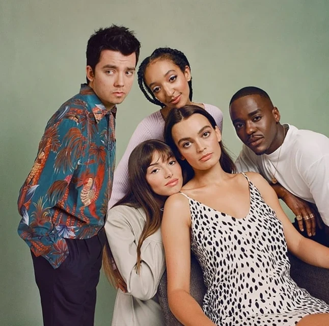 Group studio portrait of five young adult actors posing for camera against a light green backdrop wearing casual clothing, neutral expressions.
