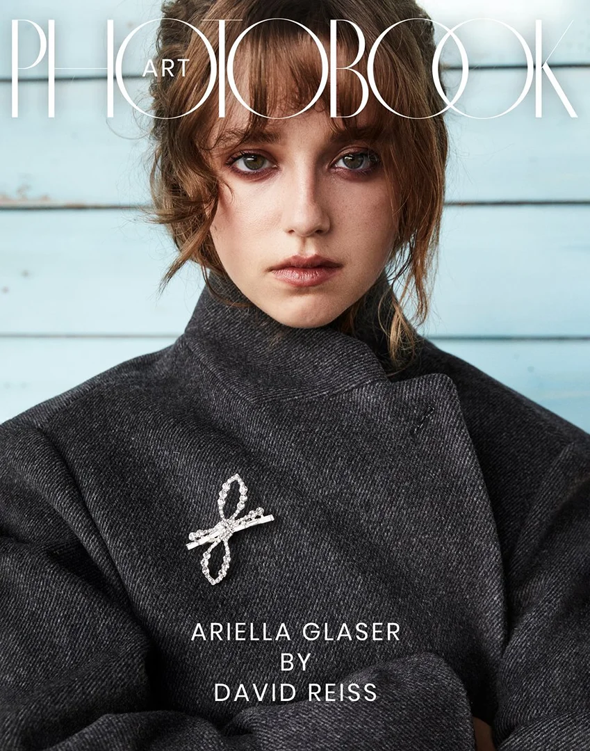 Magazine cover featuring a woman in a dark coat and a silver brooch against a light blue background with visible wood grain.