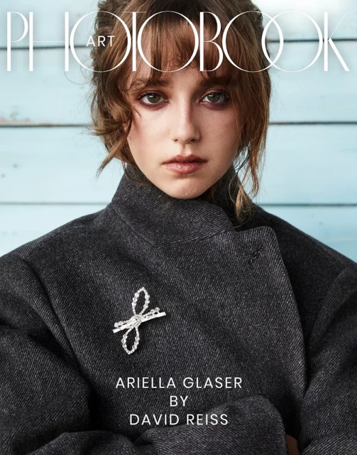 Magazine cover featuring a woman in a dark coat and a silver brooch against a light blue background with visible wood grain.