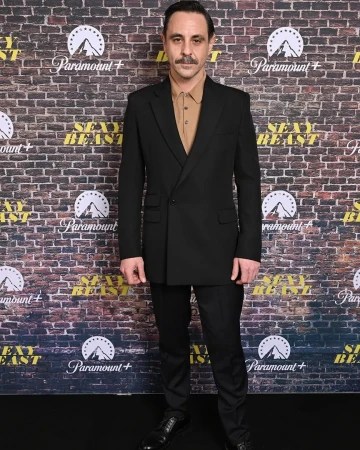 Adult male in a black suit stands in front of a brick wall with Paramount+ and Sexy Beast branding in a medium studio shot.