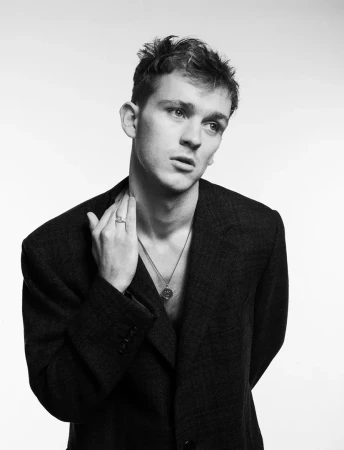 Monochrome portrait of a young man wearing an oversized blazer and a thin pendant necklace against a plain white background