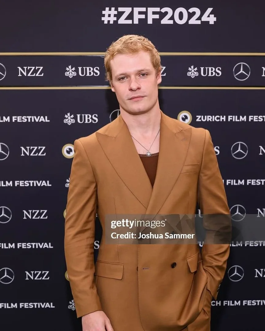 Headshot of blond male adult in a tan suit jacket at the Zurich Film Festival 2024 red carpet event in an indoor setting.
