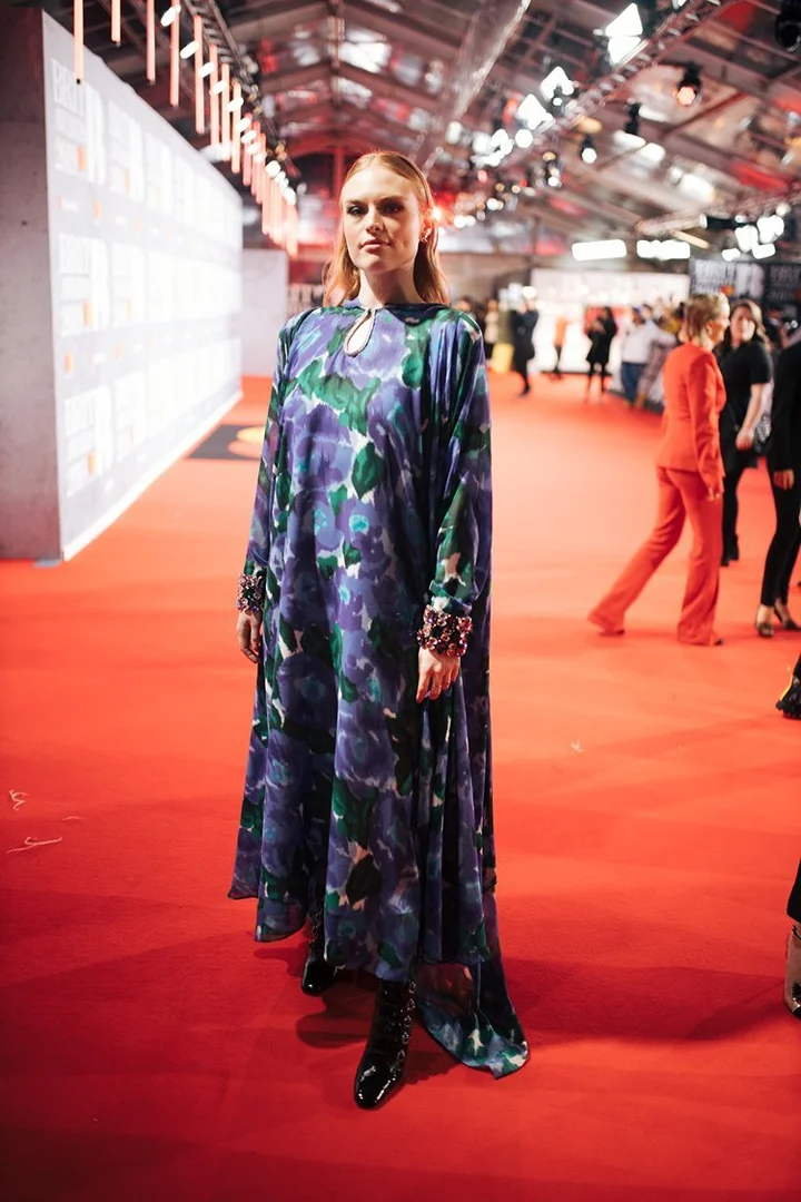 Woman in a floral-patterned gown on a red carpet at an indoor event, showcasing fashion and celebrity entertainment.