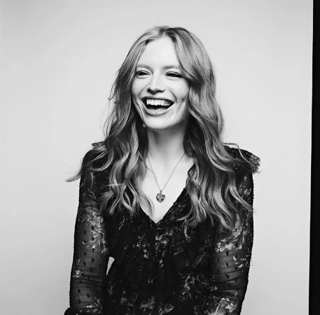 Monochrome portrait of a smiling woman wearing a dark patterned lace dress and pendant necklace against a light background