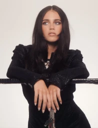 Young woman with dark hair in black textured jacket leaning on a railing against a plain background