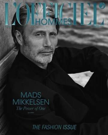 Magazine cover featuring Mads Mikkelsen in a dark jacket, striking a pose against a neutral backdrop. The title 'L'Officiel Hommes' is visible.