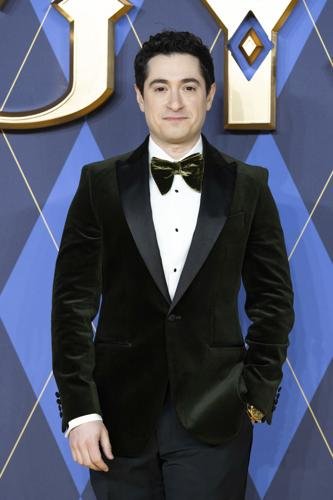 Jason Biggs poses on a blue patterned backdrop wearing a dark green velvet tuxedo jacket, bow tie, and gold wristwatch.