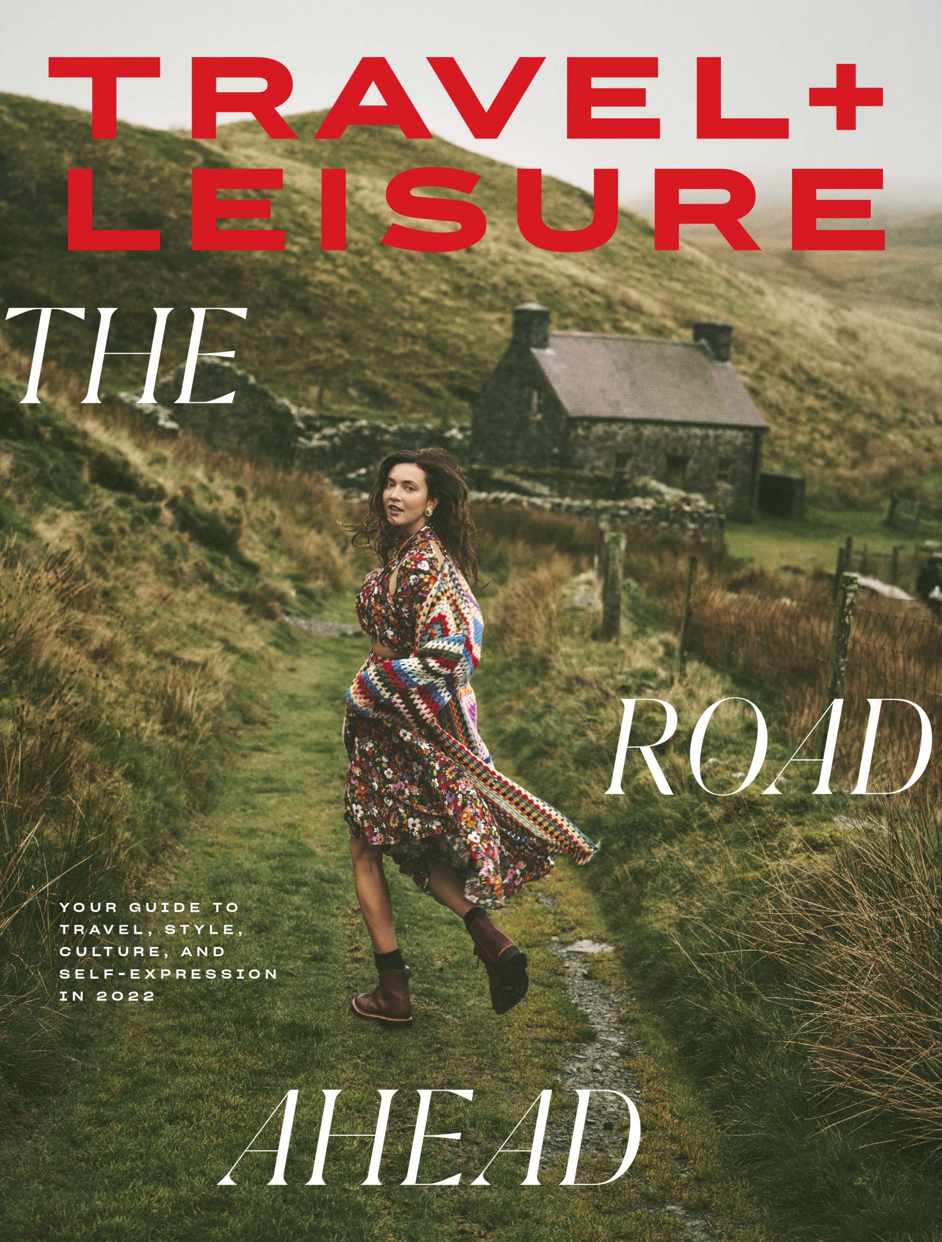 Magazine cover featuring a woman in a floral dress walking on a path in a rural landscape with a stone building in the background.